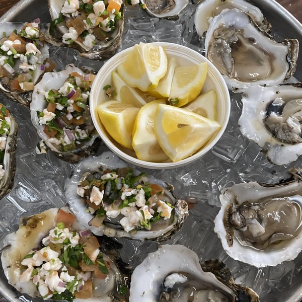 Fresh oysters on ice, some topped with ceviche, alongside a bowl of lemon wedges.
