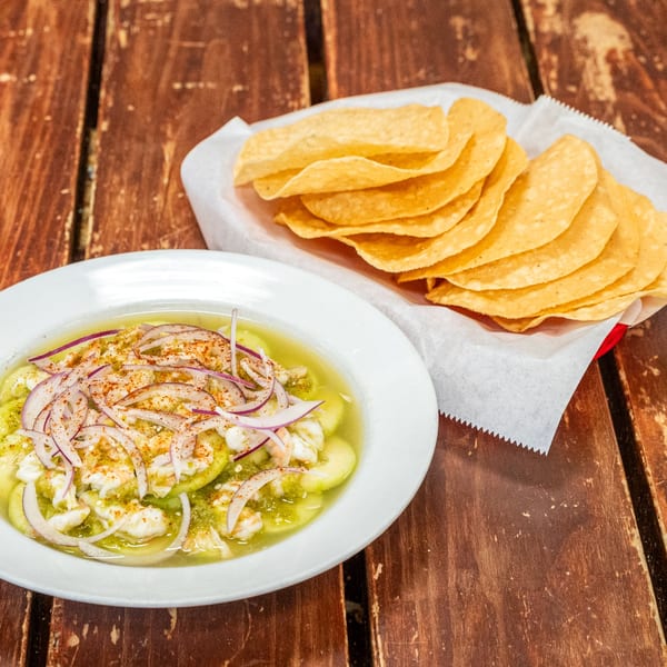 Shrimp aguachile with red onions and spices in a white bowl, alongside a basket of tostadas.