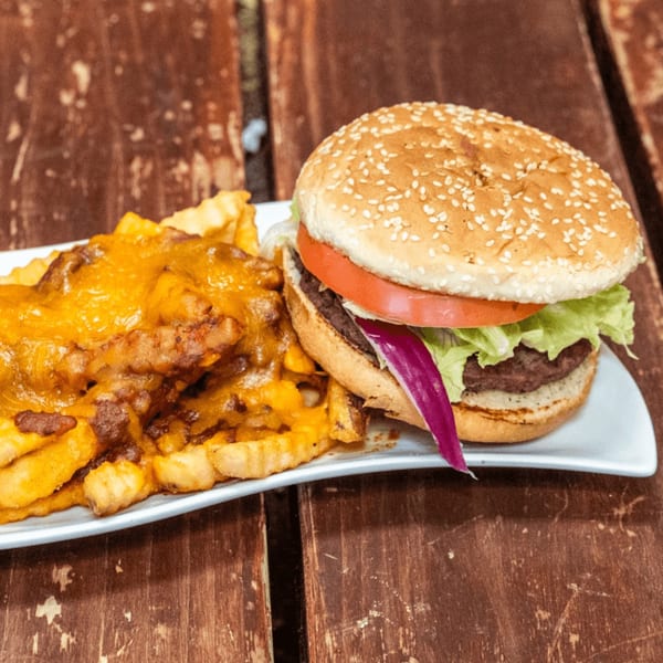 A burger with lettuce, tomato, and red onion, alongside chili cheese fries on a white plate.