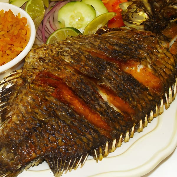 Crispy fried whole fish with a side of orange rice and a fresh salad with lime.