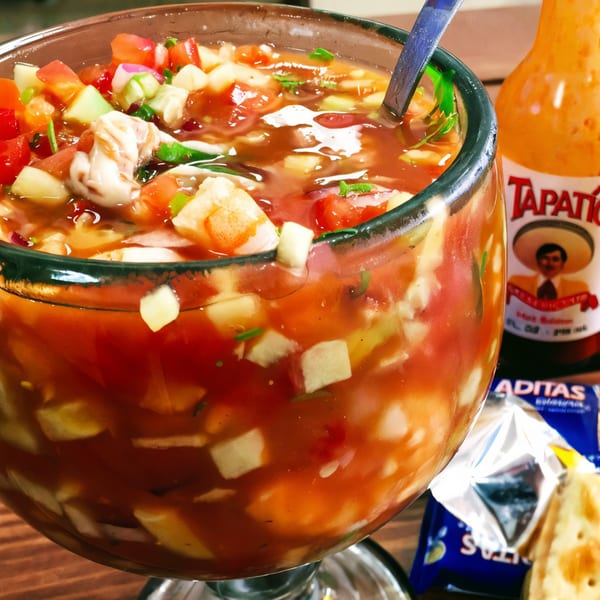A large glass of The Seafood Company's shrimp ceviche with Tapatío hot sauce and crackers.