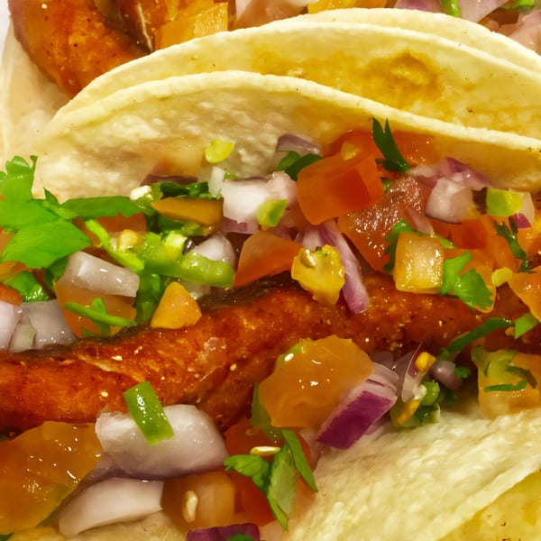 Close-up of three fish tacos with crispy fried fish, pico de gallo, and cilantro.