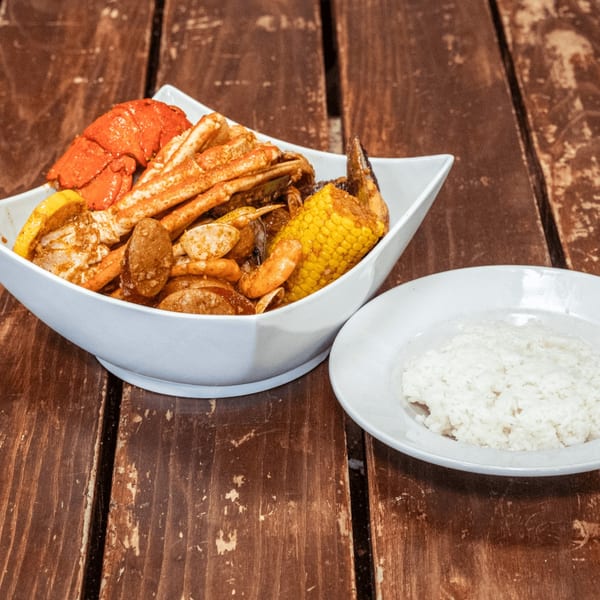 A seafood boil with lobster, crab, corn, and sausage, served with a side of white rice.