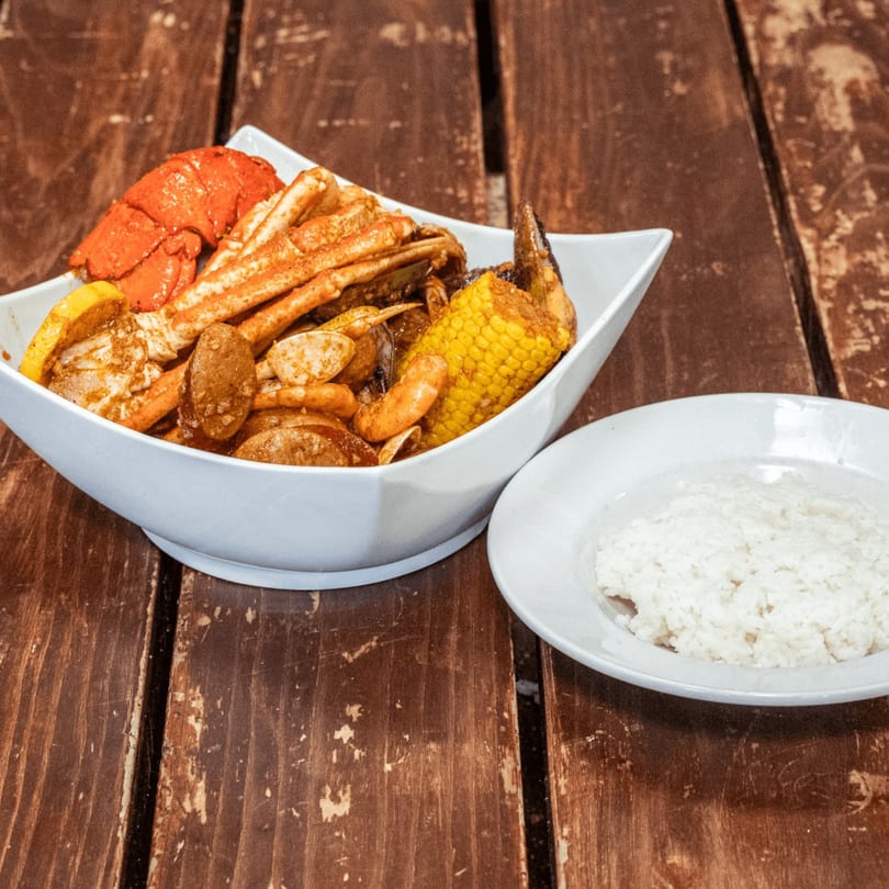 A seafood boil with lobster, crab, corn, and sausage, served with a side of white rice.