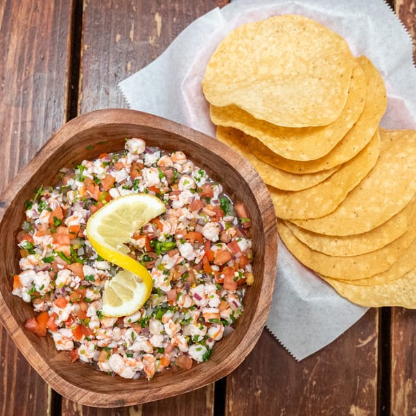 Shrimp ceviche with diced tomatoes, onions, and cilantro, garnished with lemon, served with tortilla chips.